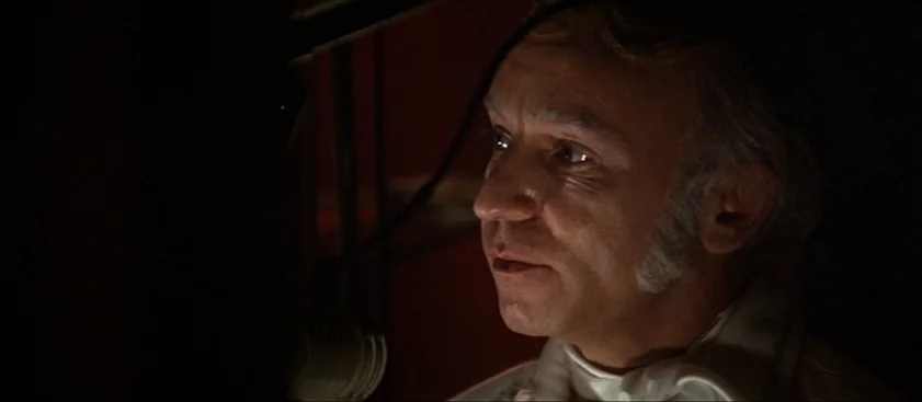 Nashville (1975) movie still: closeup — A man speaks into a microphone inside a dimly lit professional recording studio. The dark surroundings focus…