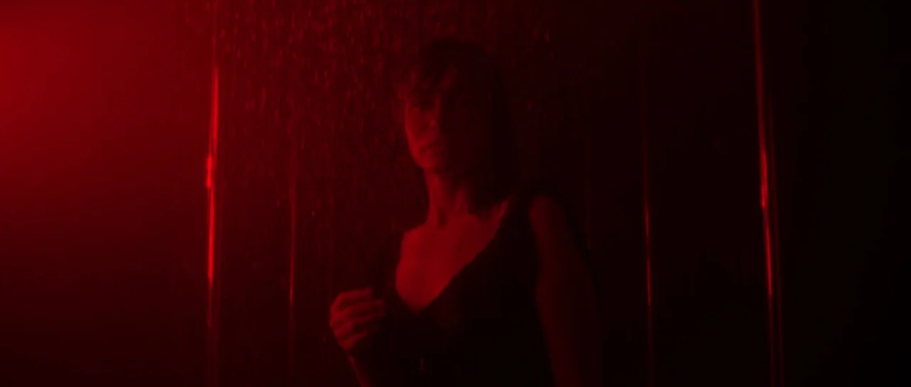 Vinyan (2008) movie still: medium — A dark, enclosed shower stall is saturated in vibrant, monochromatic red light. A woman stands under the falling…