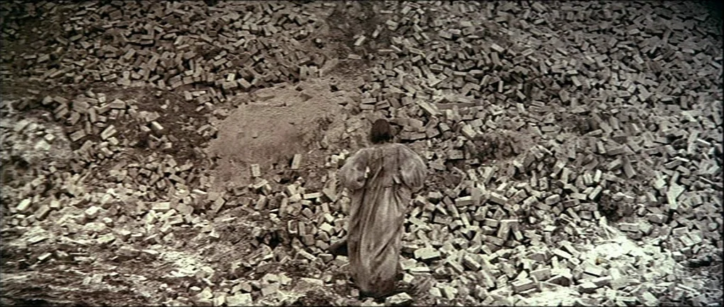 The Devils (1971) movie still: wide — A massive, sprawling heap of loose, weathered bricks fills the frame completely. A lone figure in a plain,…