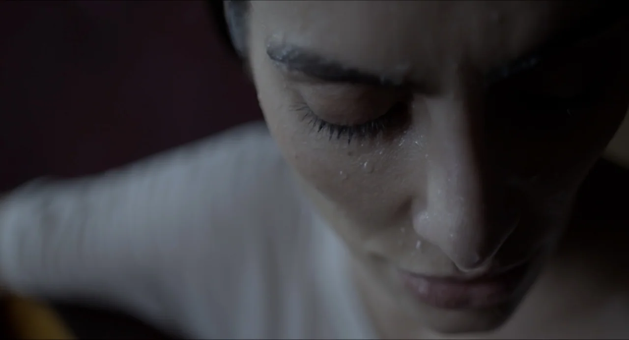 Suspension Points (2022) movie still: closeup — An interior space provides a dark, out-of-focus background for the close-up shot. A woman rests with…
