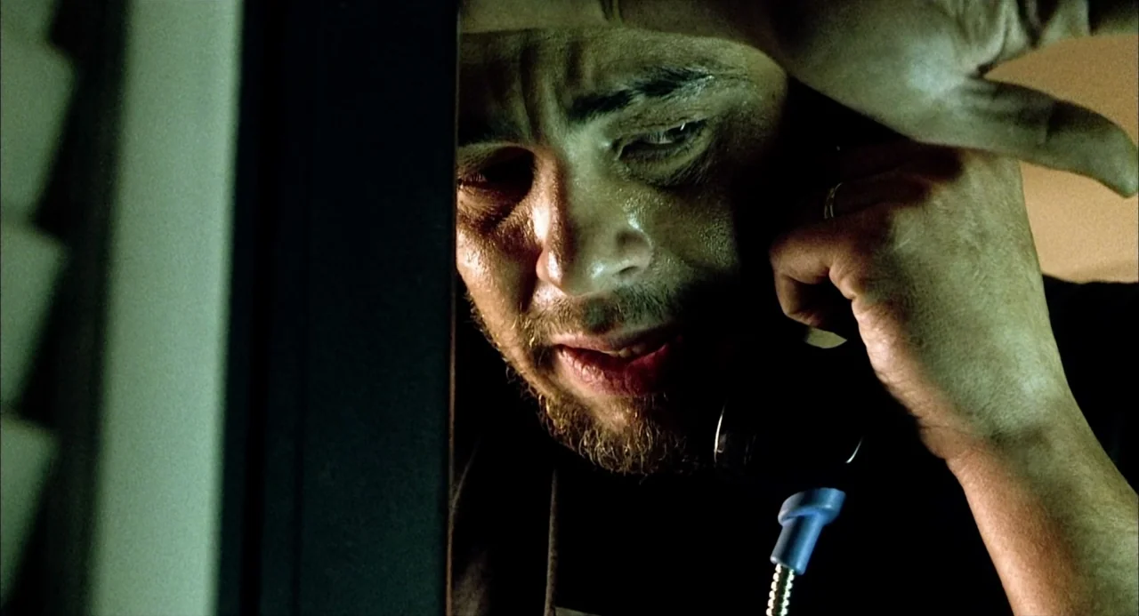 21 Grams (2003) movie still: closeup — A dimly lit, cramped telephone booth provides the setting for the shot. A man with a dark beard holds a phone…