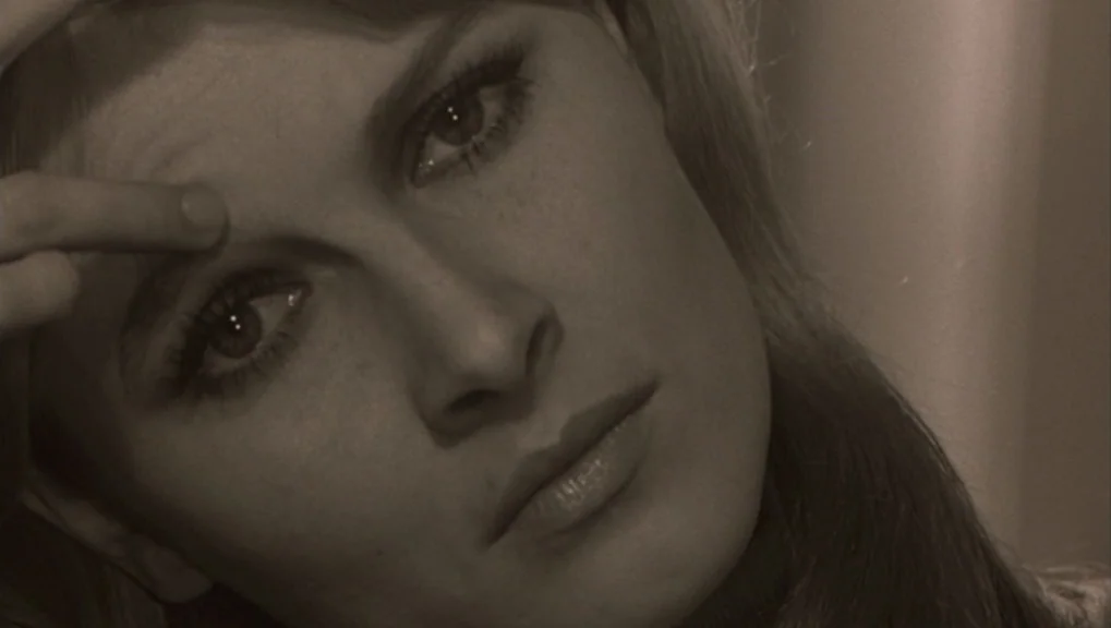 Un Homme et Une Femme (1966) movie still: closeup — A close portrait of a woman in a dimly lit interior space. A woman with dark eye makeup touches…