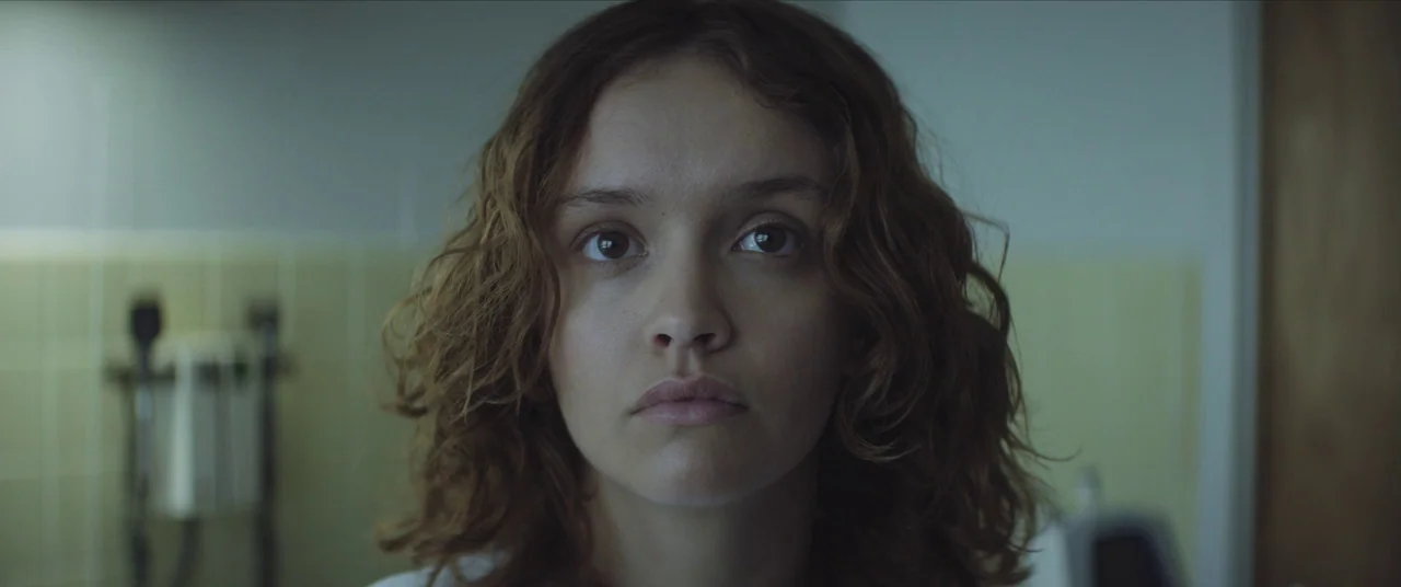 Thoroughbreds (2017) movie still: closeup — A sterile bathroom with light yellow tiles and medical equipment visible in the background. A woman with…