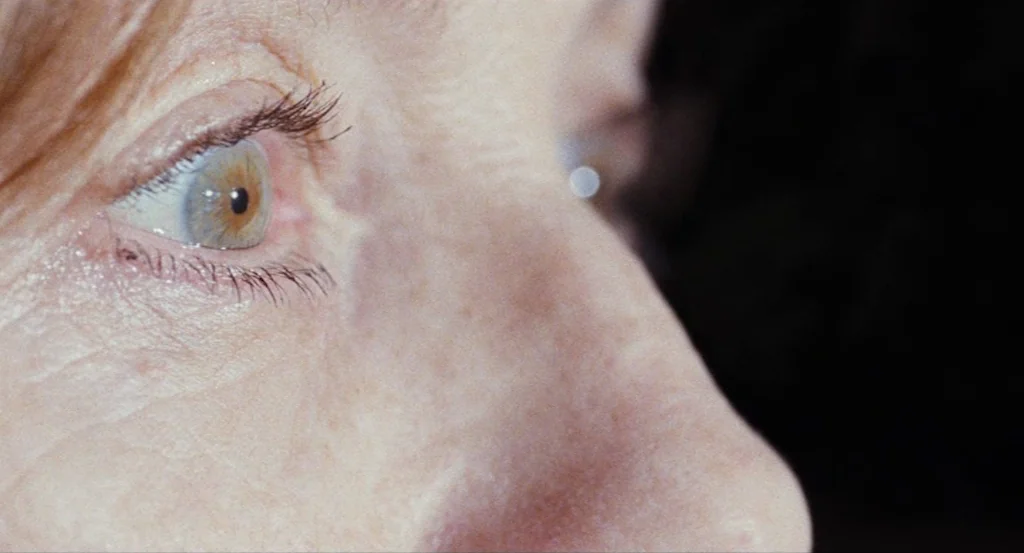 Louder Than Bombs (2015) movie still: closeup — A extreme close-up of an adult woman's face and one eye. The background is completely dark.