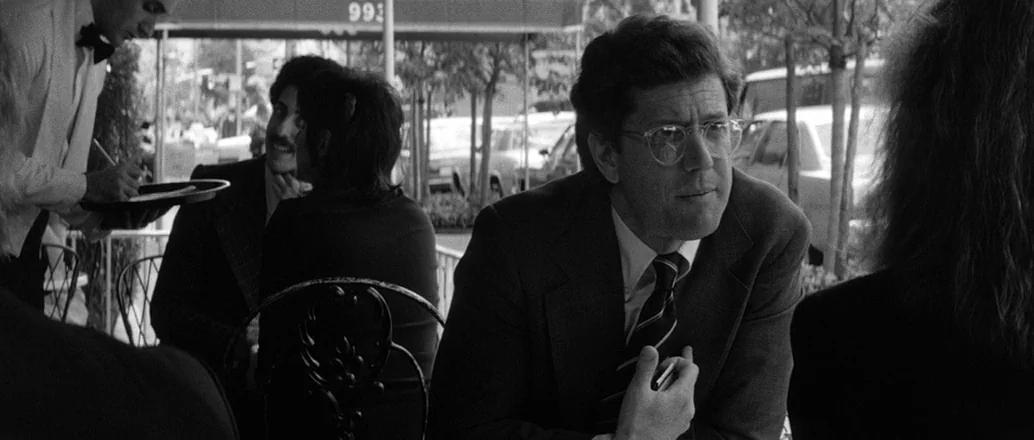 Manhattan (1979) movie still: medium — An outdoor cafe area features metal chairs and a table under a canopy. A man wearing glasses sits at the…