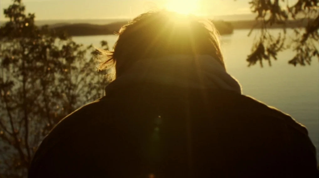 Your Sister’s Sister (2011) movie still: medium — A person stands at the edge of a lake during sunset. Bright sun glare obscures the details of the…