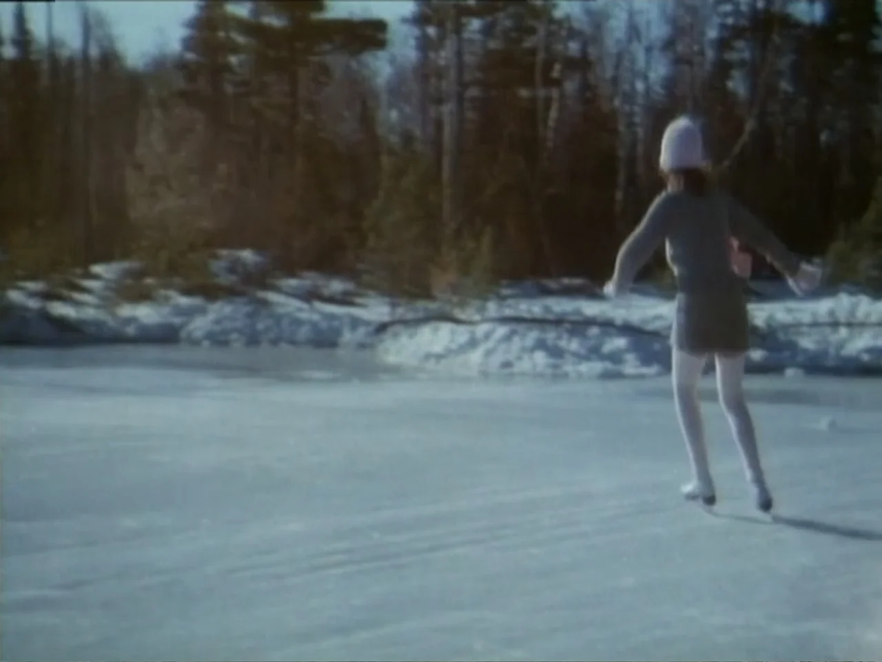 Curtains (1995) movie still: fullbody — A frozen pond surrounded by a dense, leafless forest in winter. A young woman in winter clothing glides…