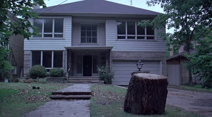 The Virgin Suicides (1999) movie still: establishing — A two-story suburban house sits in a residential neighborhood surrounded by mature trees. A…