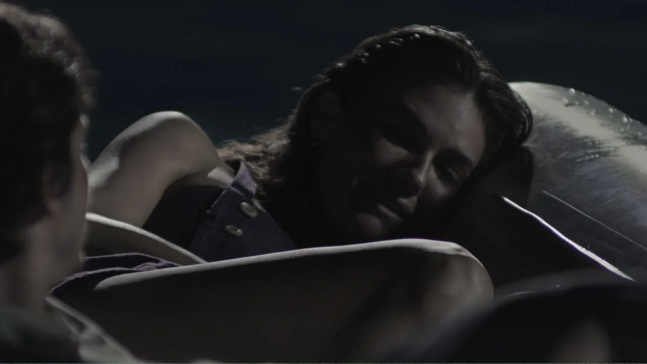Capsized: Blood in the Water (2019) movie still: medium — A dark vehicle interior with a woman lying down in the passenger seat. She looks toward a…