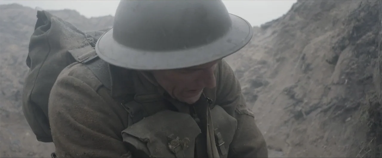 Behind the Line: Escape to Dunkirk (2020) movie still: medium — A soldier in a World War I trench stands amidst steep earthen walls. The man looks…