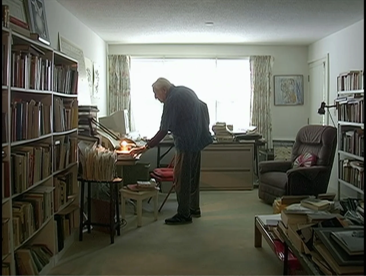 First Cousin Once Removed (2012) movie still: medium — A cluttered room lined with tall bookcases filled with various books and papers. An elderly…