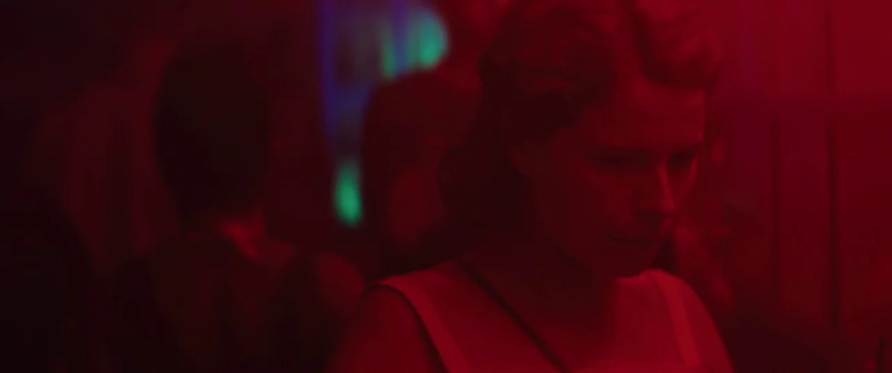 Beast (2017) movie still: medium — A dark, crowded nightclub interior is filled with red light and obscured human silhouettes. A young woman in a…