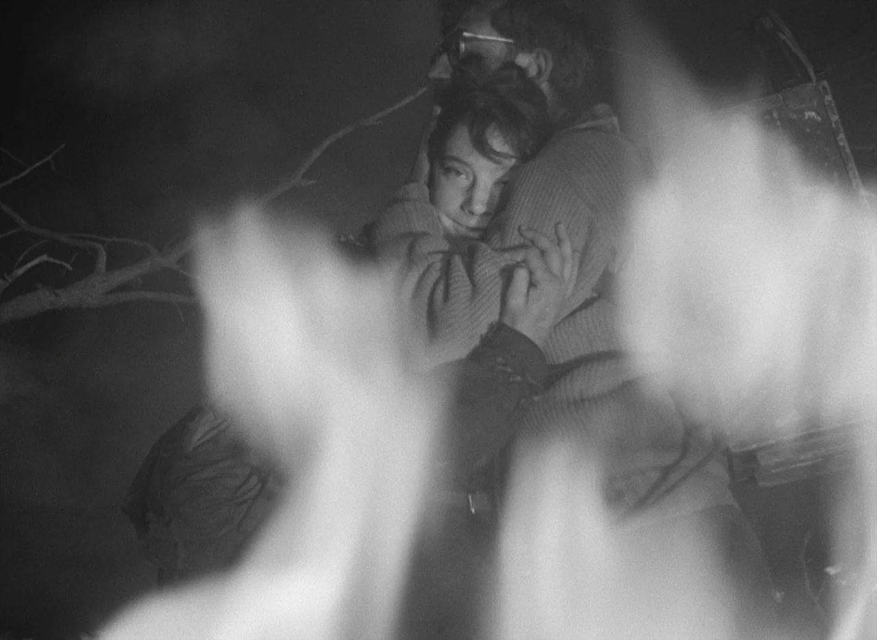 Letter Never Sent (1960) movie still: medium — A dark outdoor setting at night with out-of-focus flames in the foreground. A man and woman embrace…