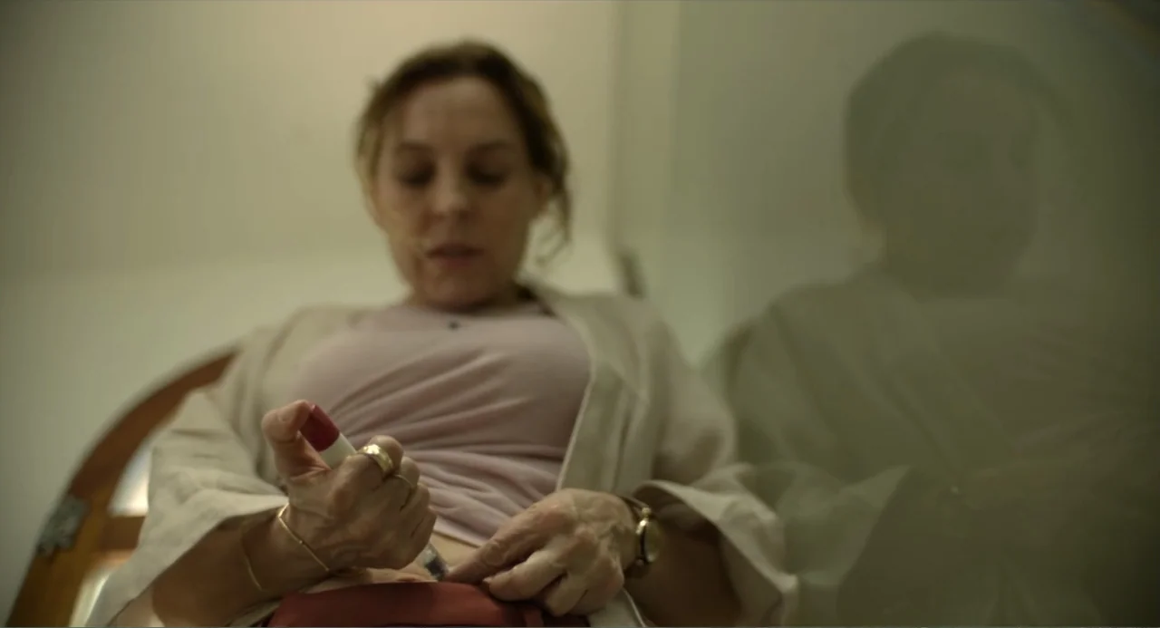 Heartbeat (2008) movie still: medium — A sterile bathroom interior features a woman standing before a mirrored surface. She uses an insulin pen to…