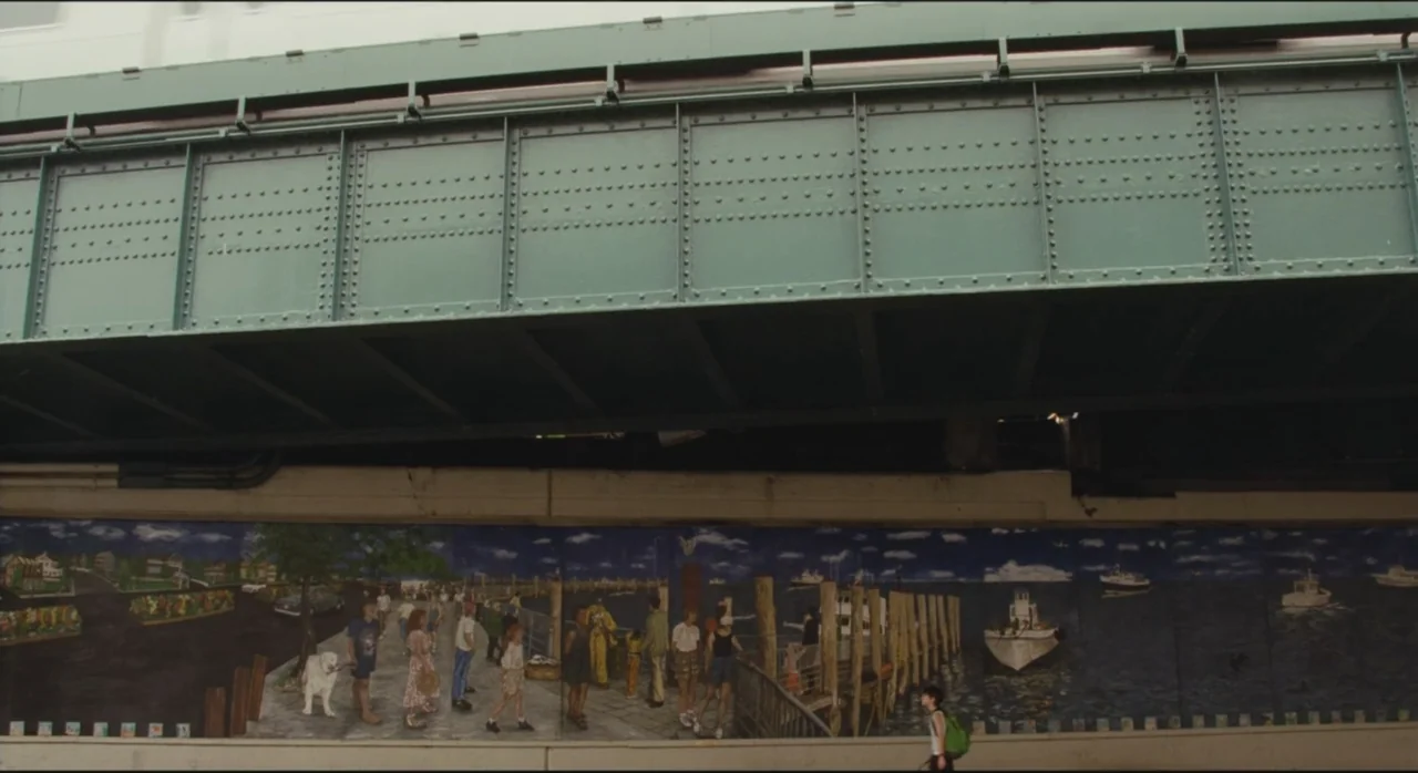 St. Vincent (2014) movie still: wide — A concrete wall beneath a metal bridge is covered with a detailed marine mural. A young child with a green…