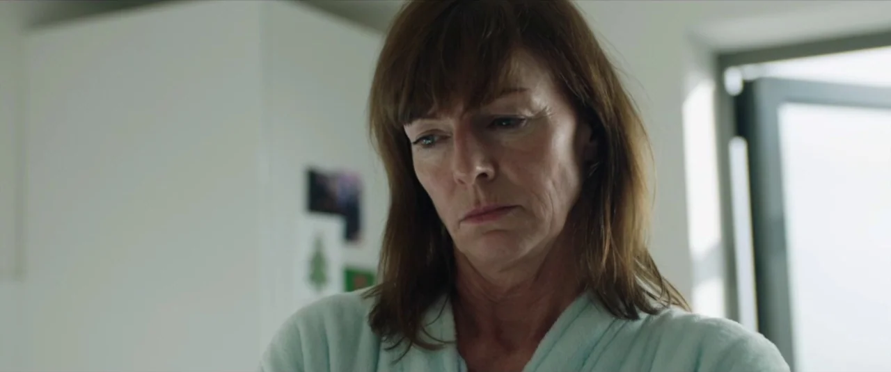 Happy New Year, Colin Burstead (2018) movie still: closeup — A woman stands in a bright room with a white wall behind her. She looks downward while…