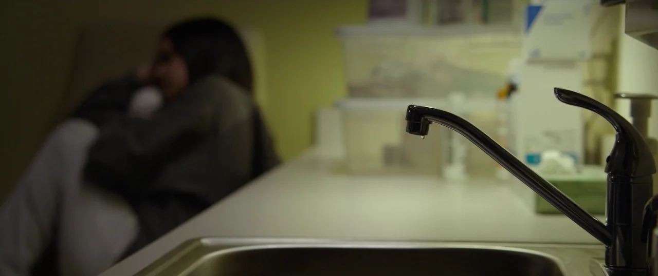 The Strangers: Prey at Night (2018) movie still: medium — A medical examination room features a chrome faucet in the foreground out of focus. A…