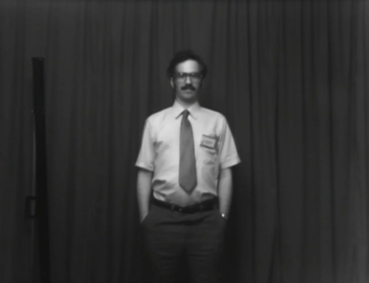 Computer Chess (2013) movie still: fullbody — A man stands centered against a dark, pleated fabric curtain. He is positioned as if for a formal…