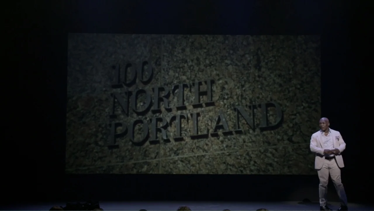 Mike Tyson: Undisputed Truth (2013) movie still: wide — A dark, expansive stage features a large projected sign reading 100 NORTH PORTLAND. A man in…