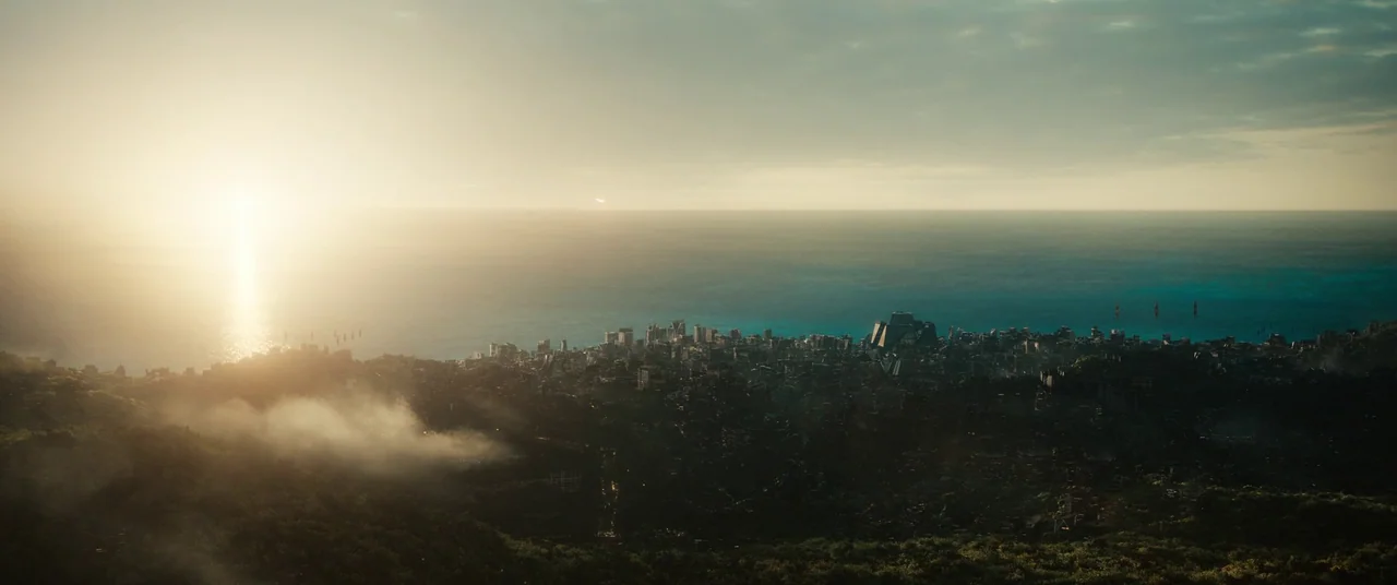 The Marvels (2023) movie still: establishing — A vast coastal city sits along the water under a clear golden sunset sky. Low-lying fog clings to the…