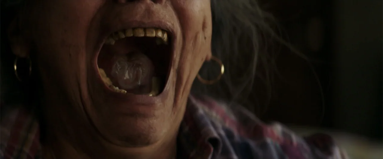 Truth or Dare (2018) movie still: closeup — A close-up shot of an elderly woman inside a dark room. The subject stands with her mouth fully open.
