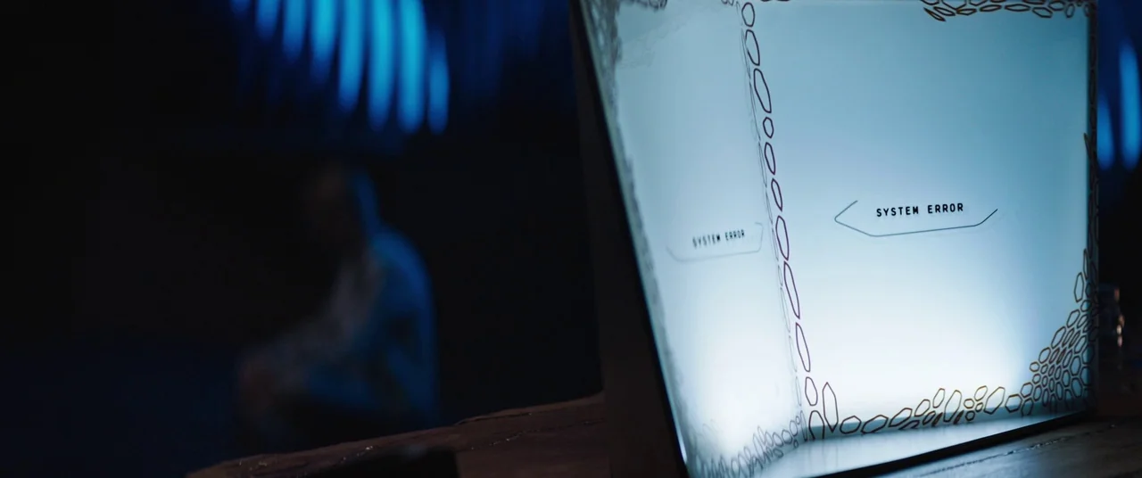 Upgrade (2018) movie still: closeup — A dark, blurred environment features a translucent screen displaying a digital error message. The screen casts…
