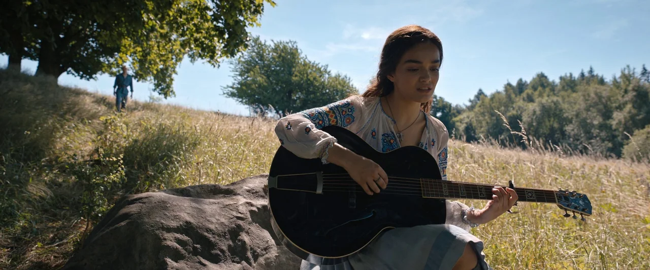 The Hunger Games: The Ballad of Songbirds & Snakes (2023) movie still: medium — A sunlit meadow features a grassy hill and large boulders under a…