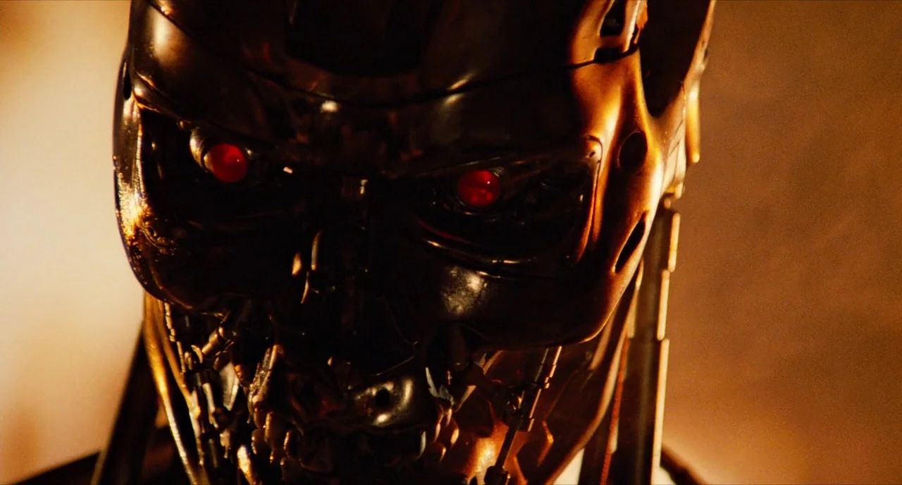 The Terminator (1984) movie still: closeup — A metallic endoskeleton skull is shown in close proximity against a dark environment. The figure glows…
