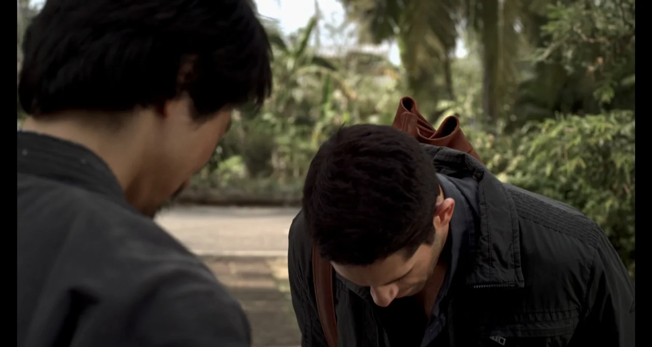 Ninja: Shadow of a Tear (2013) movie still: medium — Two men stand outdoors in a courtyard with blurred green foliage in the background. One man…