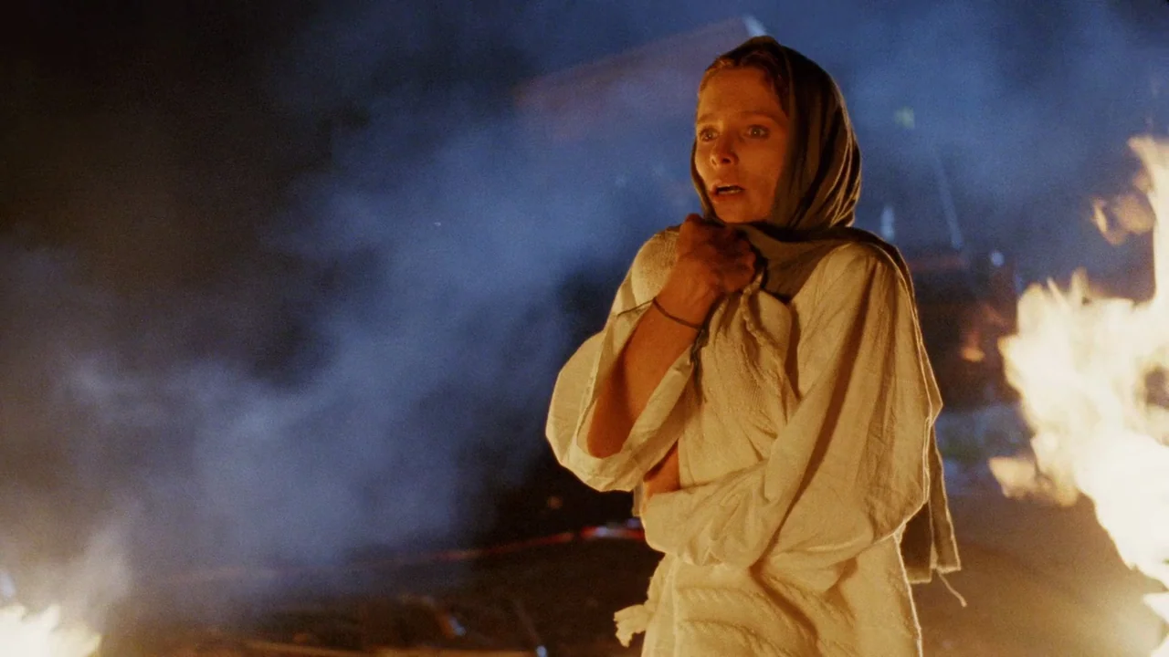 The Sect (1991) movie still: medium — A woman stands in a dark environment with thick blue smoke filling the air. She looks away from a bright fire…
