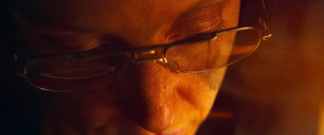 Mandy (2018) movie still: closeup — A close-up view of a person's upper face in a dark environment. The subject wears glasses and looks downward in…