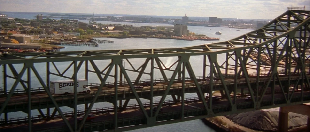 Legally Blonde (2001) movie still: establishing — A green steel truss bridge crosses over a harbor water channel in a city. Multiple cars and a…