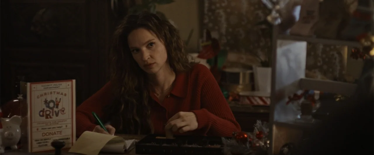 Silent Night, Deadly Night (2025) movie still: medium — A cluttered interior office space features holiday-themed donation flyers and office…