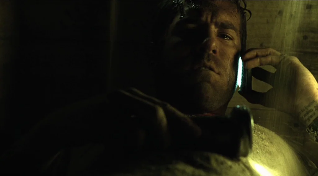 Buried (2010) movie still: closeup — A cramped, dark, wooden enclosure contains a single man lying on his back. The man holds a brightly lit…