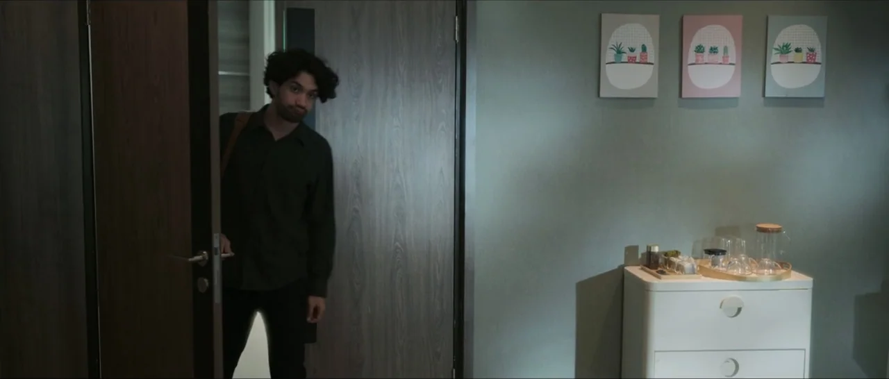 Innocent Vengeance (2023) movie still: medium — A man stands partially obscured by a wood-grain door in a quiet bedroom interior. A white dresser…