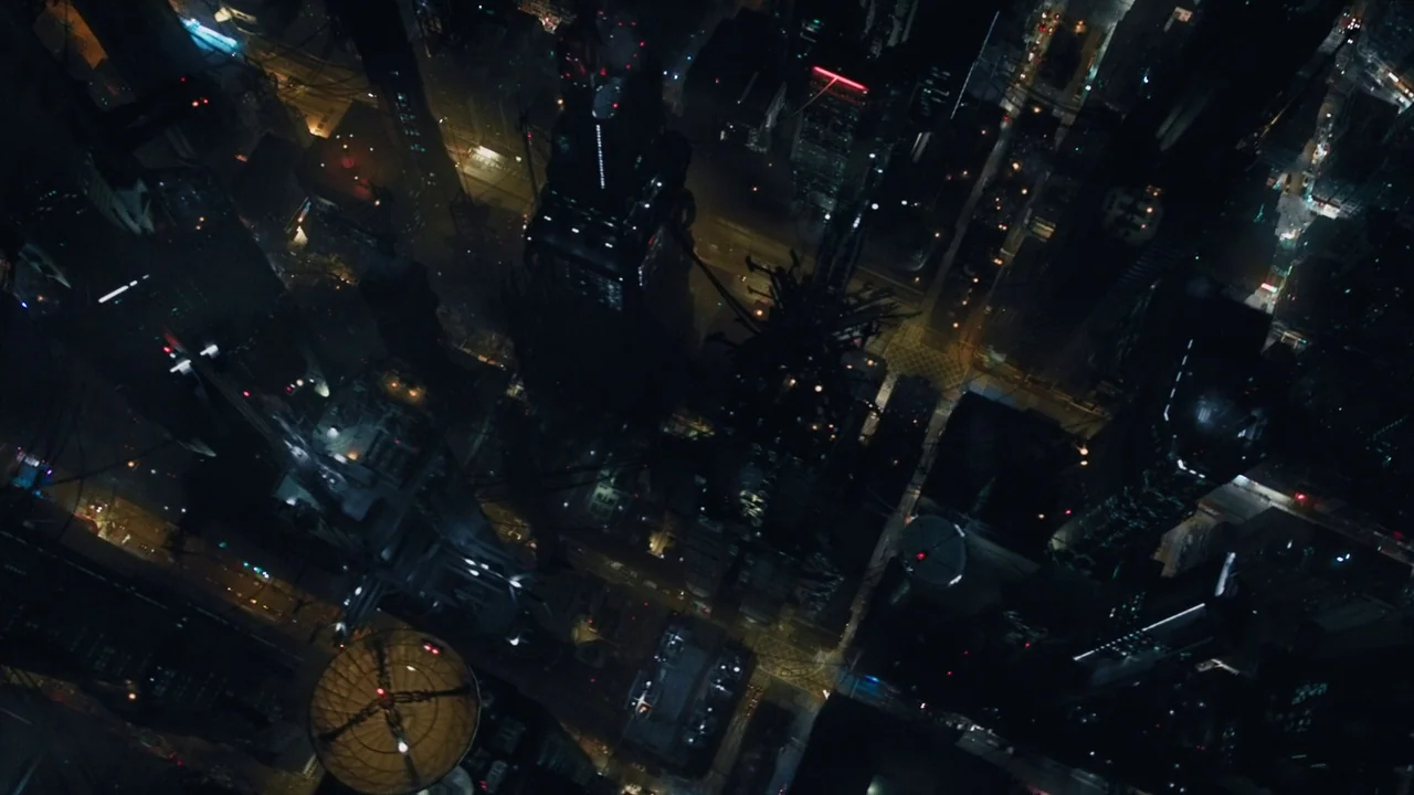 Ghost in the Shell (2017) movie still: establishing — An aerial top-down view shows a dense urban grid at night with tall structures. Streets appear…