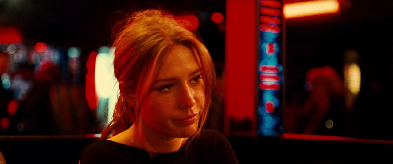 The Five Devils (2022) movie still: closeup — A dimly lit restaurant interior at night features booth seating with heavy red neon illumination. A…