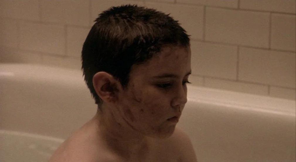 Birth (2004) movie still: closeup — A tiled alcove with white subway tiles surrounds a white porcelain bathtub. A young boy sits in the water with…