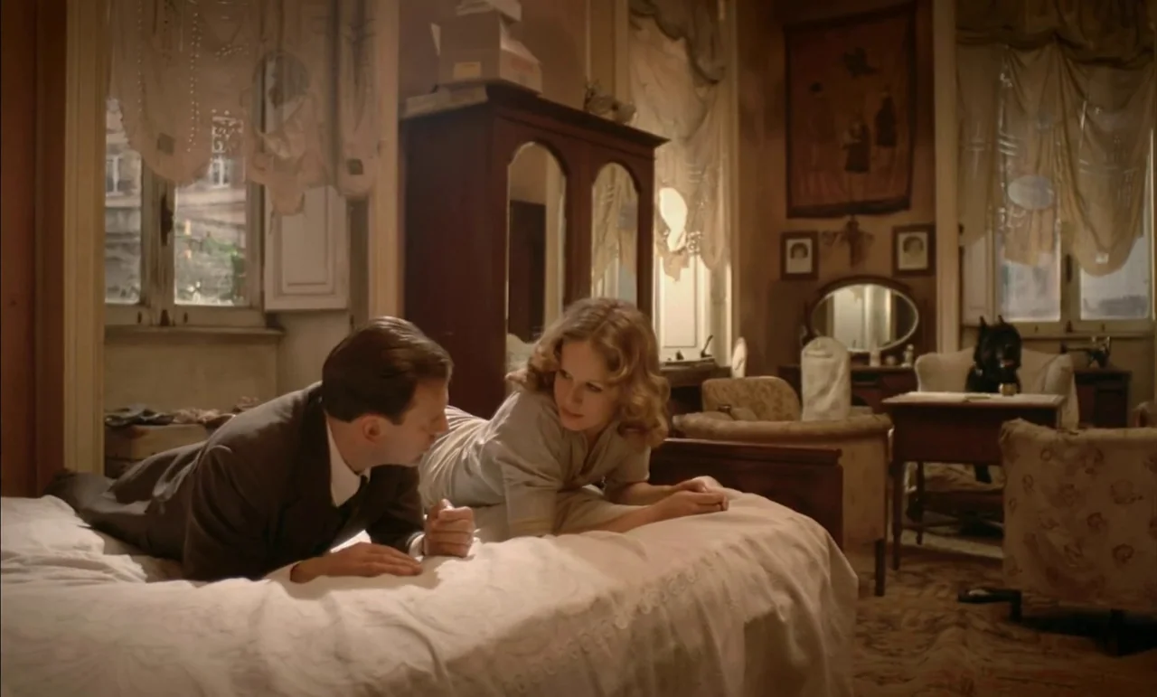 The Conformist (1970) movie still: medium — A cluttered period bedroom features tall wardrobes, sheer curtains, and ornate furniture arrangements. A…