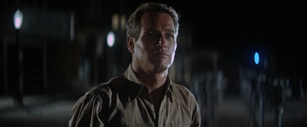 Cool Hand Luke (1967) movie still: medium — A man stands alone on a dark city street at night under distant artificial lights. The environment is…
