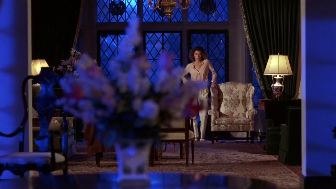 Creepshow (1982) movie still: wide — A spacious room with decorative floral patterned furniture and large leaded glass windows. A woman stands in…