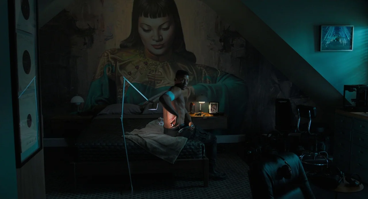 Gemini Man (2019) movie still: wide — A dimly lit room features a large, wall-filling mural depicting a woman in traditional attire. A shirtless man…