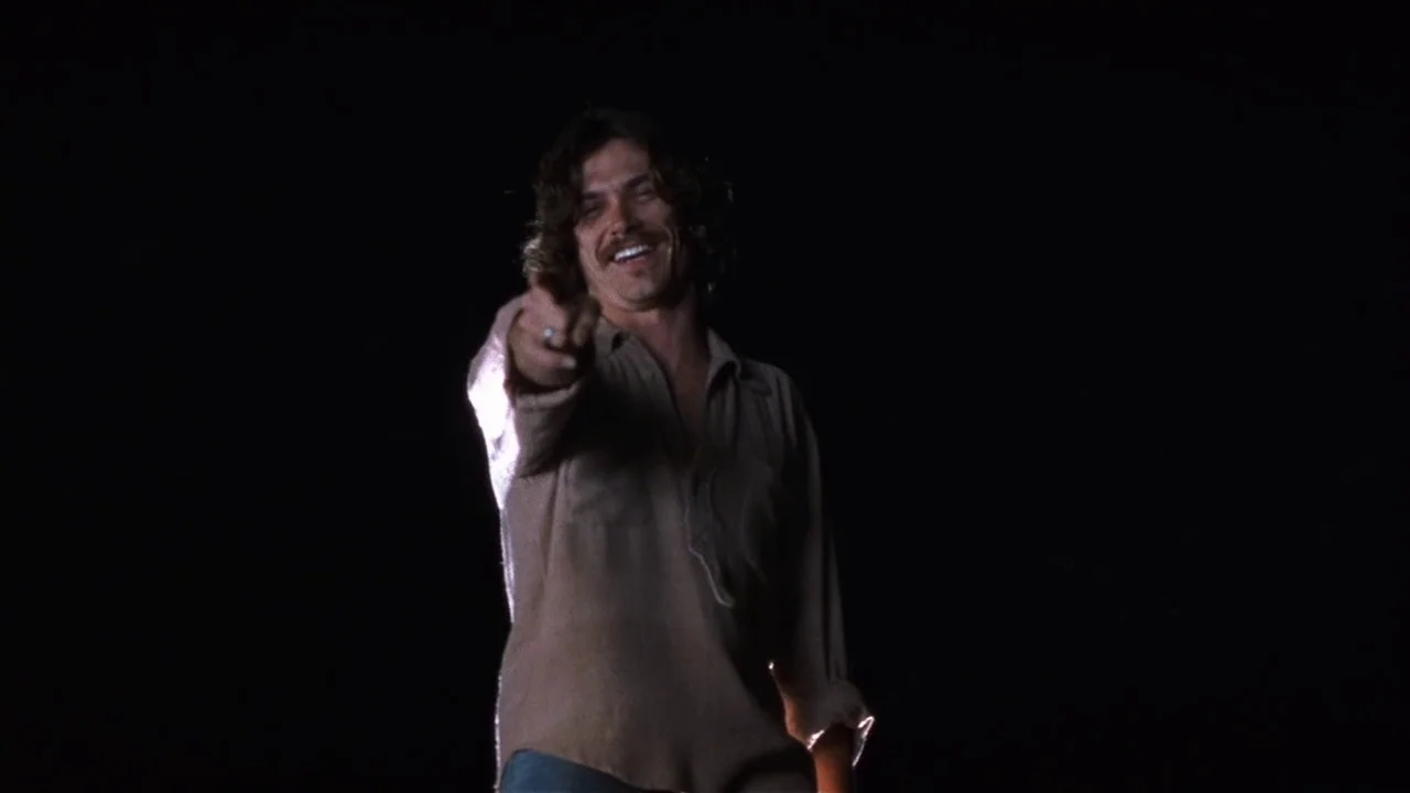 Almost Famous (2000) movie still: medium — A man stands in an environment defined by total darkness. The subject gestures toward the camera with his…