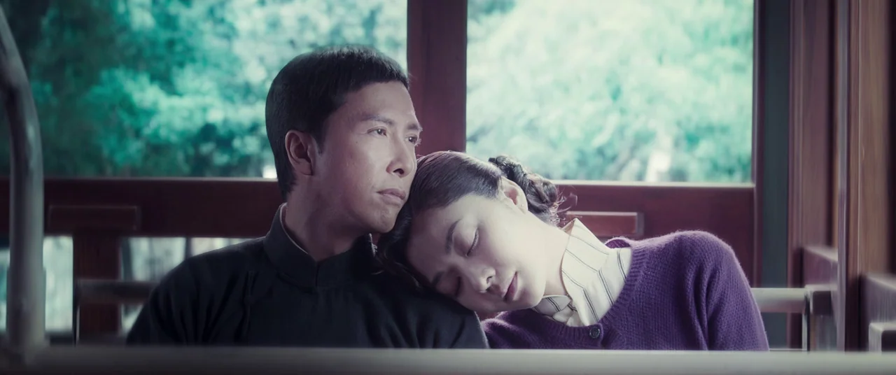 Ip Man 4: The Finale (2019) movie still: medium — The interior of a wooden-framed train car shows blurred greenery through the window panes. A man…