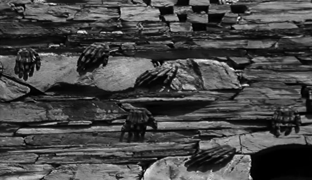 The Plea (1968) movie still: closeup — A dark, rough-hewn stone wall surface features multiple human hands embedded in the rock. The disembodied…