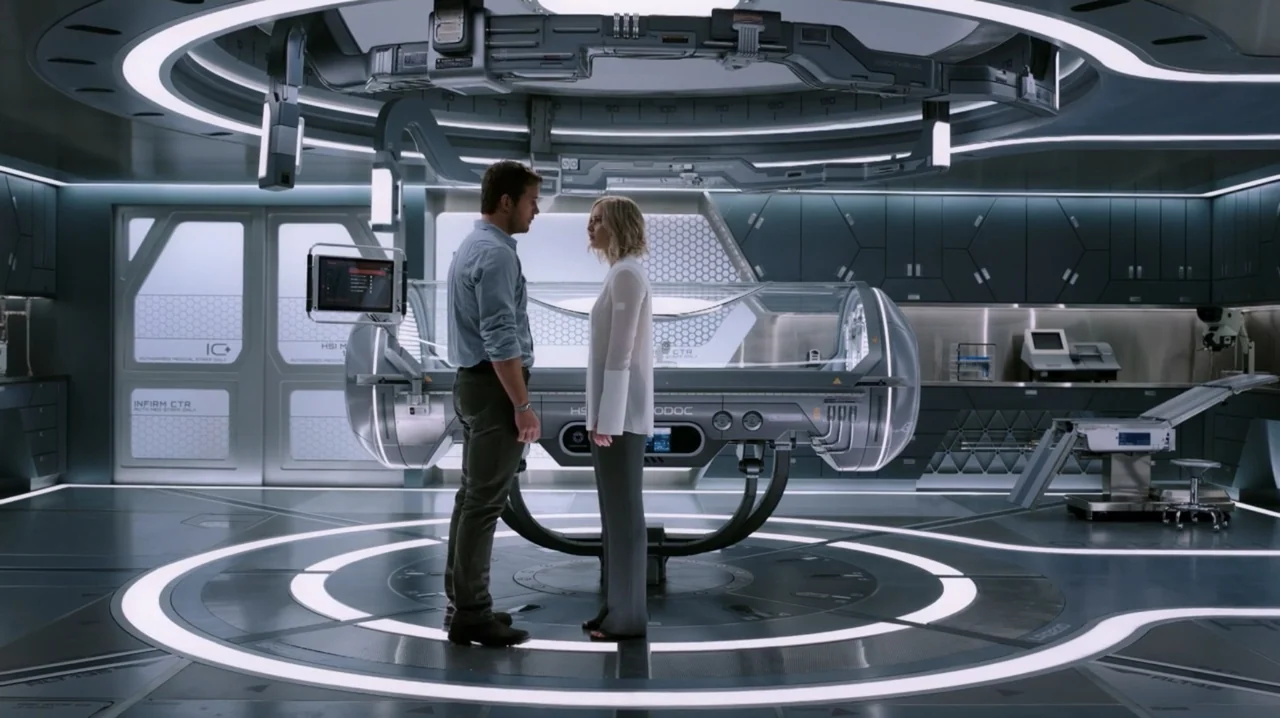 Passengers (2016) movie still: fullbody — A modern, sterile medical bay features a central glass pod and minimalist metallic walls. A man and a…