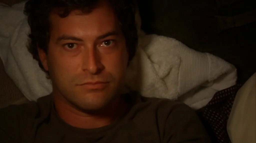 Humpday (2009) movie still: closeup — A dark bedroom features a person lying against a crumpled white towel. The subject rests on a surface while…