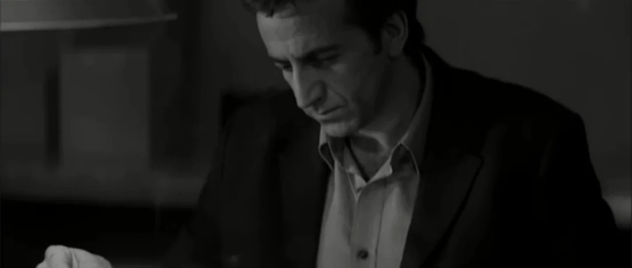 13 Tzameti (2006) movie still: medium — A dimly lit office space at night contains a desk and a working lamp. A middle-aged man in a suit jacket…