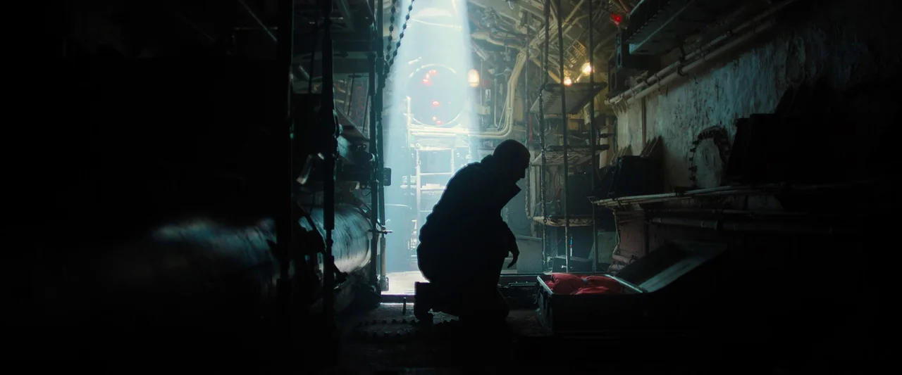 Black Sea (2014) movie still: medium — A cramped, metallic submarine corridor filled with pipes, wiring, and storage racks. A single man kneels in…