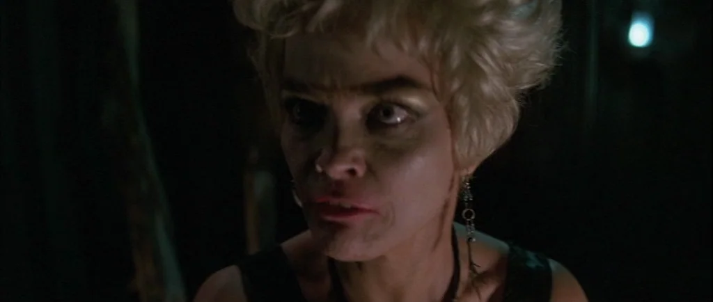 Wild At Heart (1990) movie still: closeup — A woman stands in a dark environment with indistinct surroundings. She gazes off-camera with an intense…